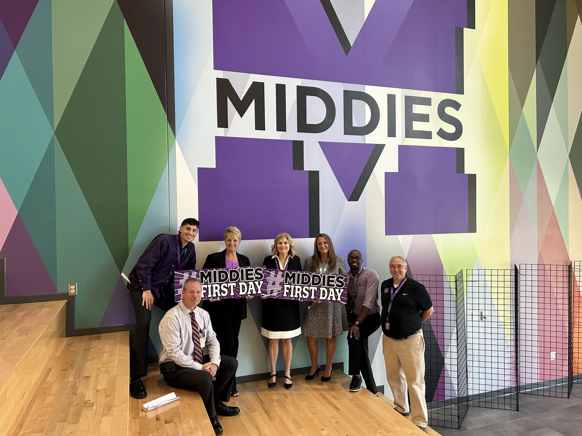 Group of 7 people posing for picture with large MCSD in the background