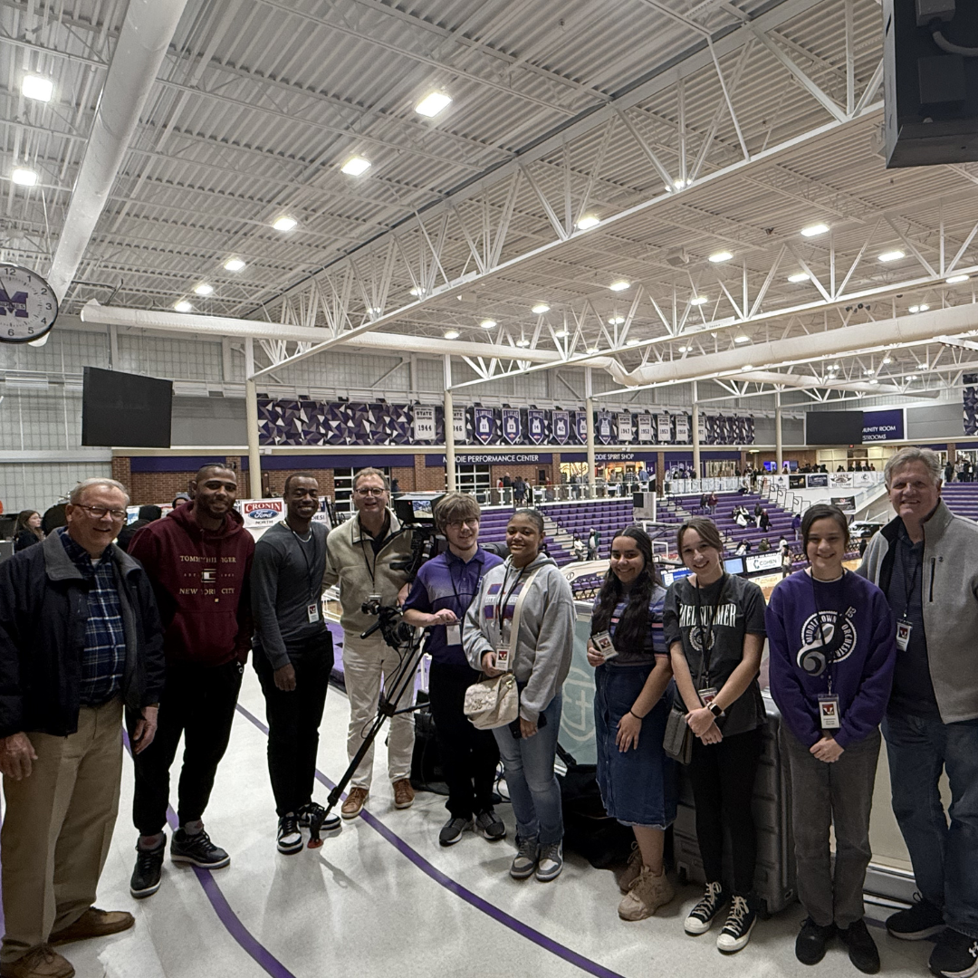 Photo shows group of people around a TV camera in the high school gym